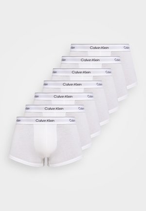 Kuusi valkoista Calvin Kleinin bokserialushousut aseteltuna porrastettuun riviin, joissa on merkitty elastinen vyötärönauha vaalealla taustalla.