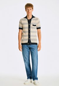 K kortärmad stickad polo med ett mönstrat, beige och marinrandigt design; har en krage, fem knappar och en bröstficka.