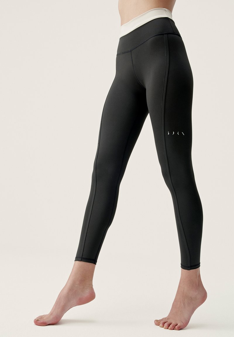 Zwarte leggings met een hoge witte tailleband, gemaakt van soepel, rekbaar materiaal en subtiele stikdetails. Klein logo op het onderbeen.