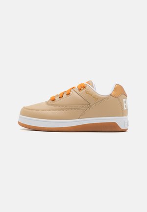 Beige sneaker with orange laces, white midsole, and gum rubber outsole. Smooth leather upper features subtle stitching and logo detail.