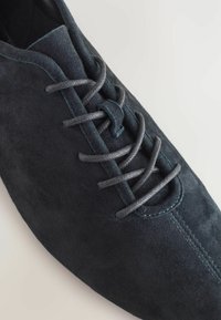 Scarpa in suede blu scuro con punta rotonda, lacci grigi scuri piatti e una superficie liscia. Un dettaglio di cucitura corre lungo il centro.