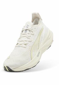 Zapatilla de malla blanca con acentos amarillos, suela acolchada y cordones. Presenta un upper texturizado y una puntera reforzada. Logotipo de PUMA visible.