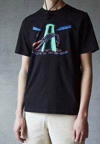 Svart bomull t-shirt med en färgglad grafik av en bil och ett grönt torn mot en blå himmel, med korta ärmar och rundad halsringning.