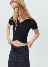 Top corto a coste di un blu navy scuro con maniche corte, caratterizzato da un design incrociato. Abbinato a una gonna fluida e fantasiosa con vita regolabile.