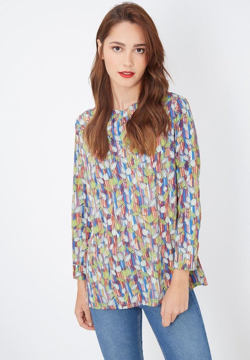 Blusa colorida con un estampado de hojas en verde, azul y rojo sobre un fondo claro, con mangas largas y un corte relajado.
