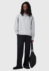 Szary sweatshirt z kołnierzykiem i logo, czarne luźne spodnie i czarne obuwie. Modelka niesie czarną torbę. Prosty, codzienny design.