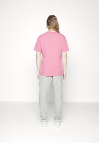 Rosa bomullströja med korta ärmar, kombinerad med gråa joggers med sidfickor och minimalistisk randig detalj.