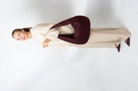 Femme en pull beige et pantalon beige tenant un grand sac tissé rouge foncé, se tenant devant un fond blanc uni.