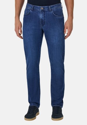 Jeans de mezclilla azul con un diseño de pierna recta, cinco bolsillos, acentos de costura y un cierre de botón. Llevados con zapatillas negras.
