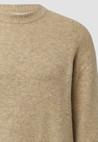 Beige gebreide trui met een geribde ronde hals, met een zachte textuur en een losvallende pasvorm, die een consistent materiaalmotief benadrukt.