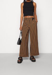 Svart crop top med åtsittande design, parat med bruna och svarta randiga vida byxor. Tillbehör inkluderar en liten svart väska och chunky sandaler.