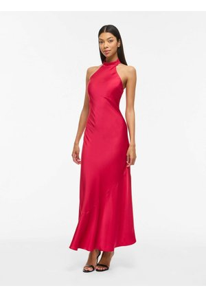 Naine põlvini ulatuvas, varrukateta punases satiin kleidis, millel on kõrge kaelus, poseerimas lihtsa valge tausta ees.