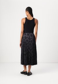 Top negru fără mâneci, combinat cu o fustă plisată neagră care are un model floral subtil. Modelul poartă pantofi negri; materialul are o textură netedă, dar cu un aspect texturat.