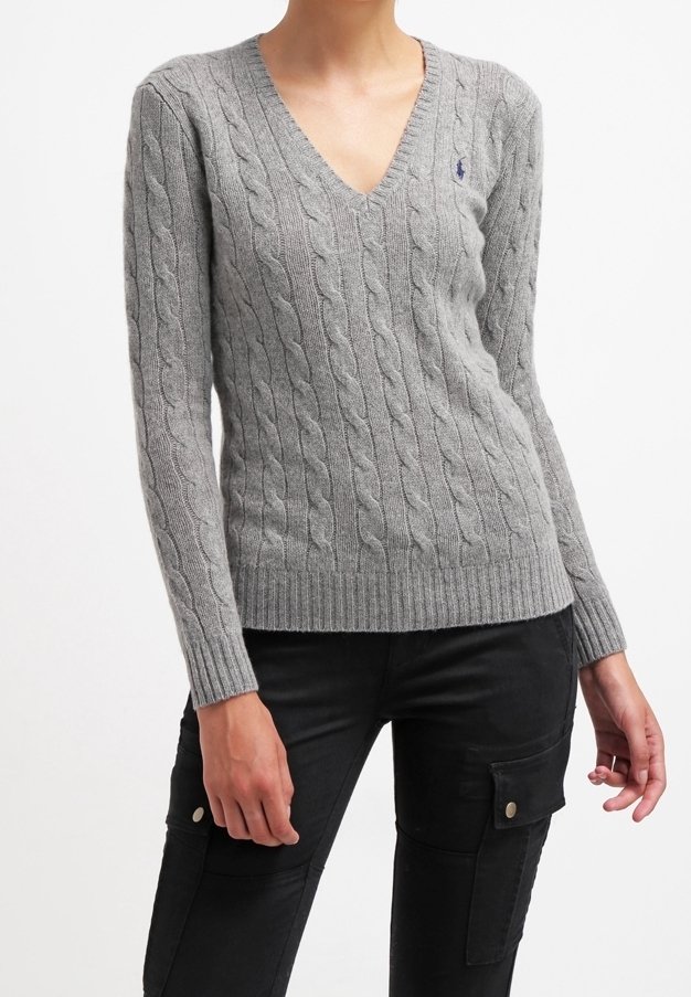 Personne portant un pull gris ajusté en maille torsadée avec col en V et un pantalon noir avec poches cargo à boutons, visible du cou jusqu'aux hanches.