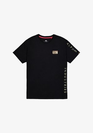 Camiseta de algodón negra con un pequeño parche decorativo en el pecho y texto en dorado que dice "ALPHA" y "INDUSTRIES" en las mangas.