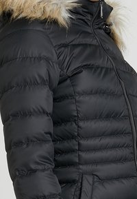 Chaqueta acolchada negra con diseño acolchado horizontal, capucha forrada de piel y cremallera frontal. Presenta un exterior liso y puños elásticos.