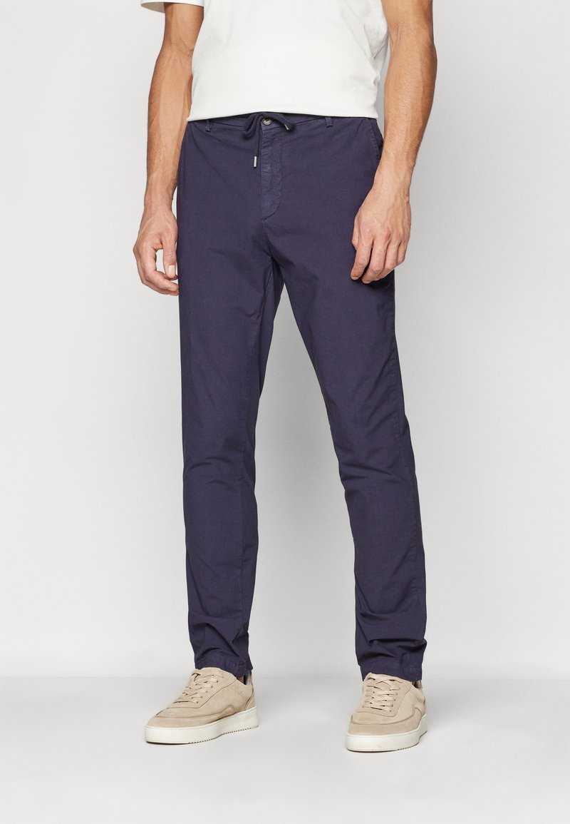 Mørkeblå bukser laget av lett stoff, med snor i livet og smale ben. Brukt med beige sneakers.