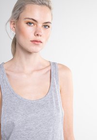 Camiseta sin mangas de color gris claro hecha de una suave mezcla de algodón. Presenta un escote redondo y tirantes anchos, con una textura lisa y sin adornos.