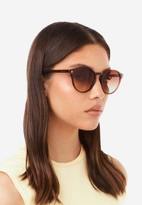 Aurinkolasit, joissa on ruskeat, pyöreät kehykset ja gradienttilinssit. Varressa on metallisia yksityiskohtia ja ruskean kilpikonnakuosiset osat.