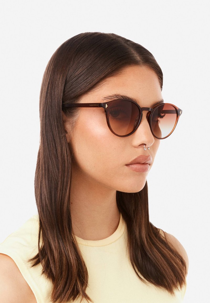 Aurinkolasit, joissa on ruskeat, pyöreät kehykset ja gradienttilinssit. Varressa on metallisia yksityiskohtia ja ruskean kilpikonnakuosiset osat.