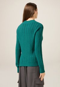 Grün gestrickter Pullover mit langen Ärmeln und geripptem Saum. Das strukturierte Design weist horizontale Rippen und einen runden Ausschnitt auf.