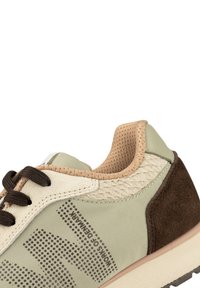 Sneaker verde chiaro con tacco in suede marrone, dettagli perforati color crema, lacci marroni, motivo del logo e mesh testurizzato attorno al colletto.