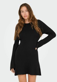 Robes en tricot côtelé noir avec manches longues, ourlet festonné, silhouette ajustée et poches latérales. Texture douce et design polyvalent.
