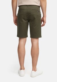 Pantalones cortos verde oliva de corte recto, hechos de una tela ligera. Con dos bolsillos traseros y una textura suave, combinados con zapatillas blancas.