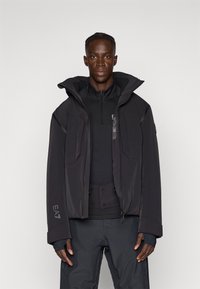 Schwarze isolierte Jacke mit hohem Kragen, Frontreißverschluss und großer Kapuze. Verfügt über mehrere Taschen und eine strukturierte Innenschicht.