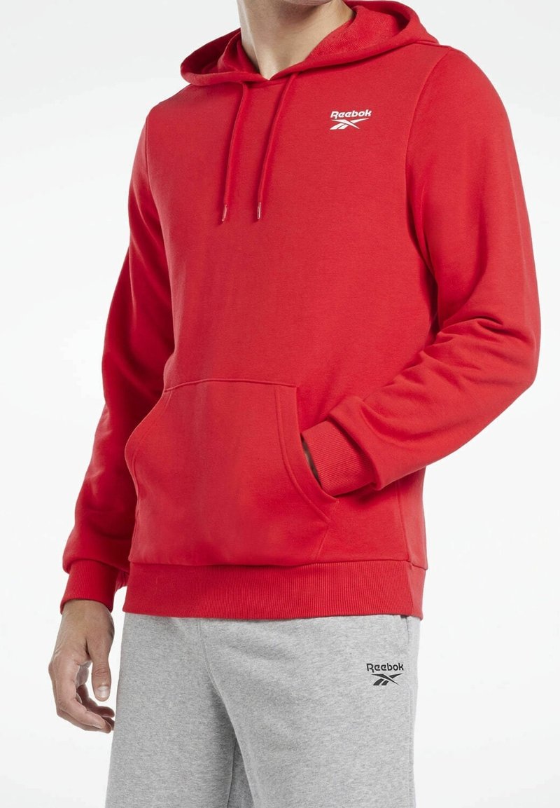 Haut à capuche rouge Reebok avec une poche frontale, un cordon de serrage, des poignets côtelés et un logo sur la poitrine. Tissu doux avec une texture lisse.