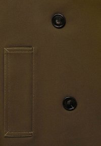 Brown fabric with visible rectangular pocket stitching and two black four-hole buttons arranged vertically.