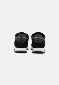 Czarne buty sportowe z teksturowaną cholewką, z zamszowymi akcentami i białymi podeszwami. Charakteryzują się brandingiem "Calvin Klein" na pięcie oraz gładkim designem.