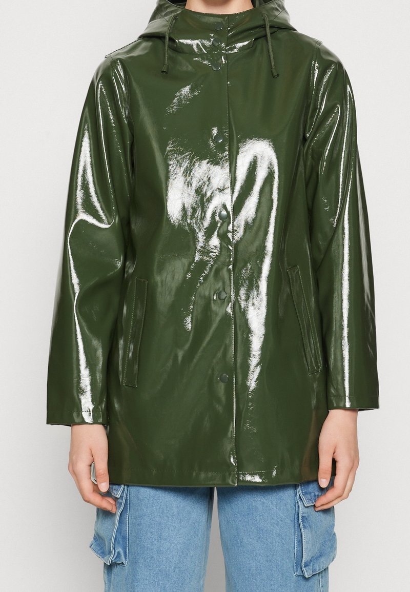 Skinande grön vattentät regnjacka med huva, framknappar och sidofickor. Tillverkad av ett glättat, reflekterande syntetmaterial.