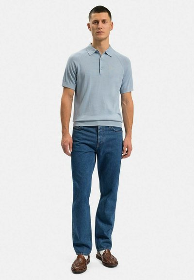 Ljusblå kortärmad polo med krage, tillsammans med mörkblå raka jeans och bruna flätade slip-on skor.