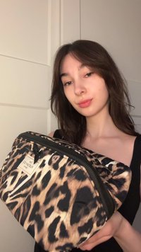 Trousse de maquillage à imprimé léopard avec fermeture éclair. Texture en tissu doux, présentant des motifs noirs et bruns. Une étiquette attachée affiche le nom de la marque.