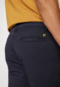 Pantaloni blu navy con un design elegante, realizzati in un tessuto morbido. Presentano un piccolo logo giallo ricamato sulla tasca posteriore.