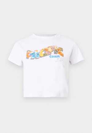 Camiseta blanca recortada con texto colorido "Pacific Coast" que presenta gráficos florales y de playa en el frente.