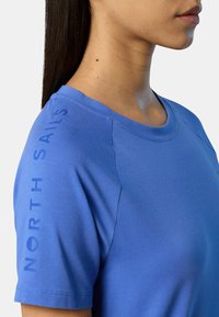 T-shirt corto blu a maniche corte realizzato in tessuto liscio, con la scritta "NORTH SAILS" stampata verticalmente sulla manica sinistra. Collo arrotondato e design aderente.
