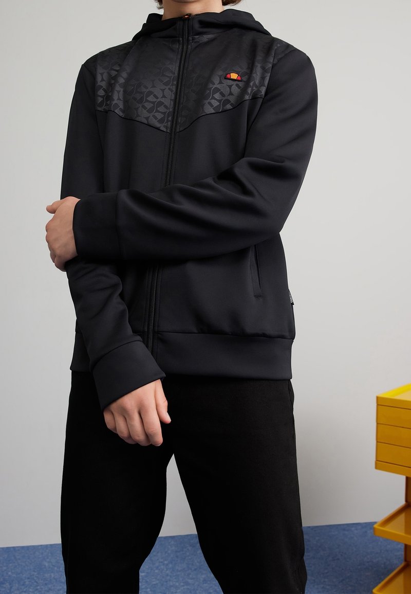 Black zip-up hoodie with a textured chest panel. Features a hood, side pockets, and ribbed cuffs. Logo at left chest area.