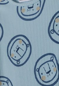 Svijetloplava rebrasta tkanina sa ponovljenim ilustracijama lica lava u tamnoplavoj boji, uz bež akcentima za facialne karakteristike.
