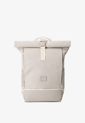 Beige roll-top backpack with front buckle, side pockets, and bottom zipper compartment, featuring a "Johnny Urban" logo patch.