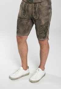 Bruna skinnshorts med dekorativ broderi, med hög midja och sidofickor, kombinerade med vita sneakers.