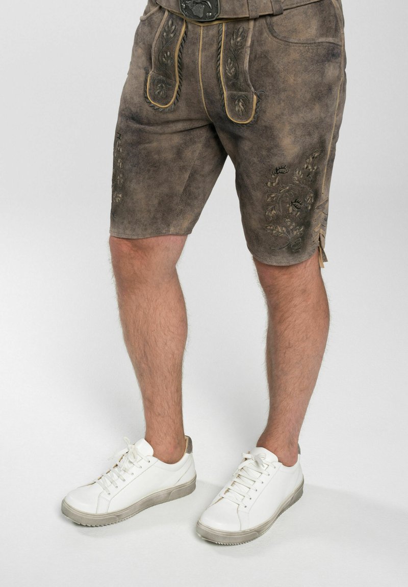 Bruna skinnshorts med dekorativ broderi, med hög midja och sidofickor, kombinerade med vita sneakers.