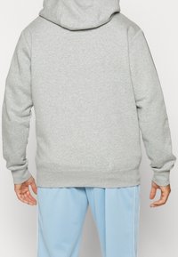 Grå huvtröja med långa ärmar, ribbade muddar och nederkant, i blandning av bomull, avslappnad passform, bärs över ljusblå byxor.