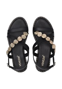 Schwarze Leder-Sandalen mit überkreuzten Riemen, goldenen Münz-Akzenten und Nieten entlang der Kanten. Flacher Sohlensohle, verstellbarer Knöchelriemen und Markenlogo.