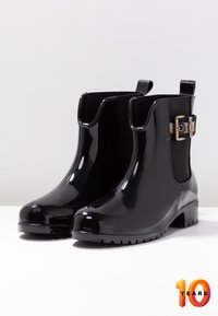 Botas de tobillo de goma negras con acabado brillante, paneles laterales elásticos y detalle de hebilla con acentos dorados. Suela de goma texturizada para un buen agarre.