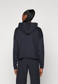 Sudadera recortada en color marino, fabricada con una mezcla de algodón, que cuenta con una capucha grande, mangas largas y un ajuste relajado. Detalles elásticos en los puños y el dobladillo son visibles.