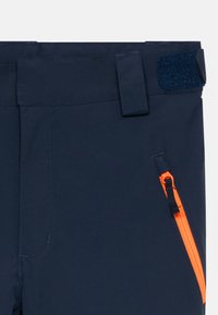 Temno modri hlače z oranžnim diagonalnim zadrgo žepom, zanko za pas in zapiranjem na ježka na pasu.
