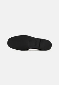 Black shoe sole, smooth textured rubber with a slight curve at the heel and a branded area. Minimalist design, no intricate patterns or accents.
