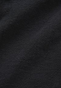 Black fabric with subtle textured diamond pattern and slight folds creating soft shadows and depth.